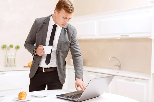 Businessman standing with cup of coffee using computer — Stock Photo, Image