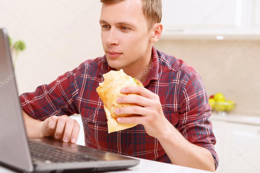 Man eating sandwich in front of computer