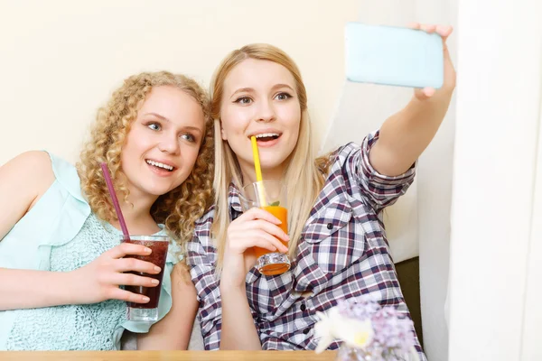 Две улыбающиеся девушки делают селфи в кафе — стоковое фото