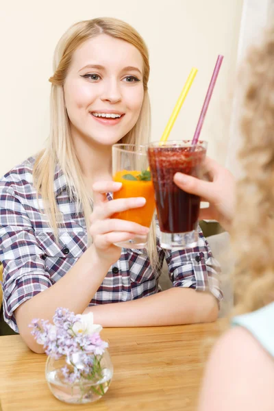 Two women clinking glasses with cocktails in cafe