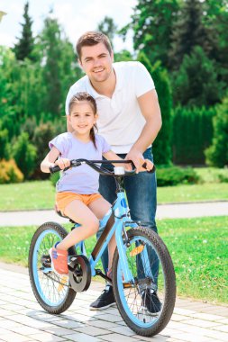 Father teaching daughter to ride a bike clipart
