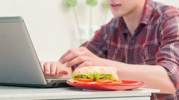 Close-up man eating sandwich in front of computer — Stock Video