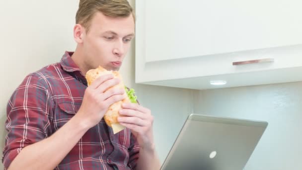 Primer plano del hombre comiendo sándwich y sosteniendo el ordenador portátil — Vídeos de Stock