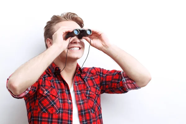 Interested smiling guy looking through binoculars — Stock Photo, Image