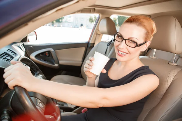 Glimlachende zakenvrouw in auto met kop koffie — Stockfoto