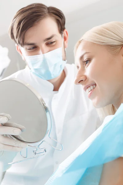 Smiling woman looking in mirror by dentist — Stock Photo, Image