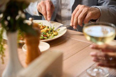 Erkek, bir restoranda bir masada, arkadaşının yanında bir bardak şarapla yemek yiyor.