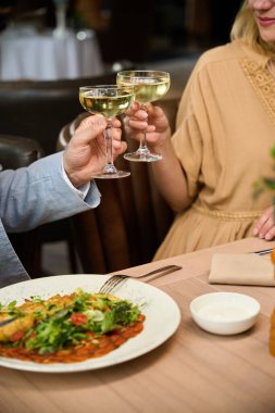 Lokantada bir bardak şarapla bir kadın ve bir erkek, tabakta lezzetli yemekler.