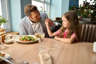 Kızları baba salatasını besliyor, bir restoranda bir masada oturuyorlar.
