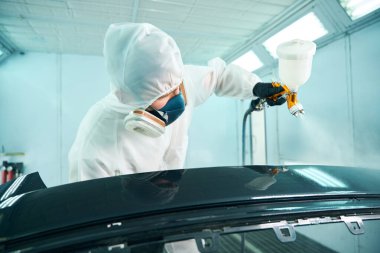 Araba tamirhanesinde araba kaportasında sprey tabanca boyası kullanan koruyucu kıyafetli bir tamirci. Araba servisi konsepti