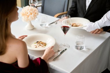 Genç bir adamla kadının restoranda buluşurken çekilmiş bir fotoğrafı. Garson masaya salata koyuyor. Romantizm, tarih, ilişki kavramı