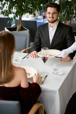 Mutlu çift restoranda buluşmanın tadını çıkarıyor. Garson sofraya yemek koyuyor. Romantizm, tarih, ilişki kavramı