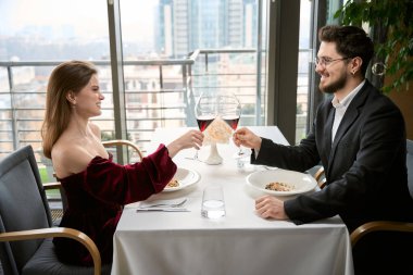 Lokantada kutlama yaparken kadeh tokuşturan mutlu genç bir çift. Birbirlerine bakıyorlar. Romantizm, tarih, ilişki kavramı