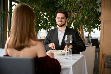 Gözlüklü genç adam restoranda yemek yerken kadına bakıyor. Romantizm, tarih, ilişki kavramı