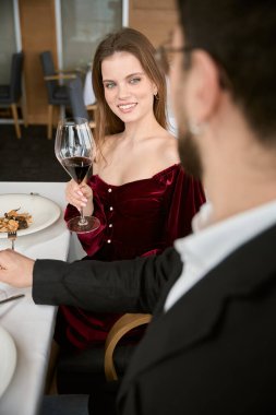 Randevu sırasında elinde kırmızı şarapla restoranda erkek arkadaşına bakan neşeli bir kadın. Romantizm, tarih, ilişki kavramı