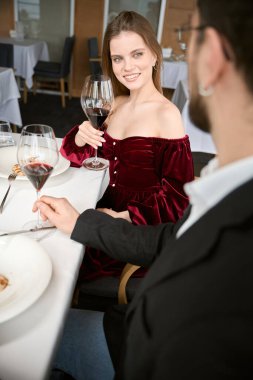 Restoranda buluşurken elinde kırmızı şarapla gülümseyen genç adam ve kadın. Romantizm, tarih, ilişki kavramı