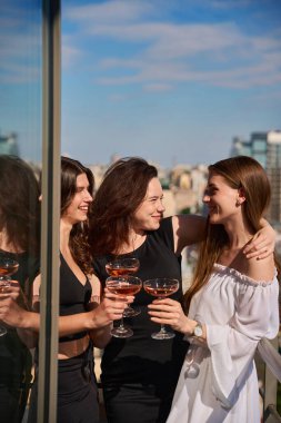 Mutlu genç kadınlar terasta şampanya bardaklarıyla kadeh kaldırırken kucaklaşıyorlar.
