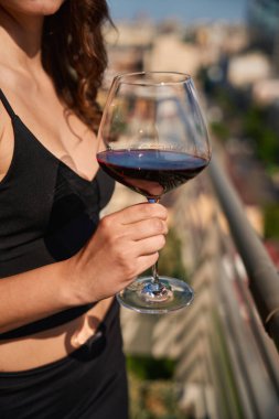 Terasta kırmızı şarap ve cam tutan bir kadının kesilmiş fotoğrafı.