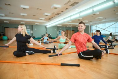 Jimnastik sopalarıyla spor salonunda yere uzanan gülümseyen kadın ve erkekler. Fitness, spor, eğitim, spor salonu ve yaşam tarzı konsepti