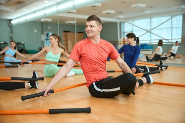 Sportif erkekler ve kadınlar spor salonunda yerde esnerken jimnastik çubukları kullanıyorlar. Fitness, spor, eğitim, spor salonu ve yaşam tarzı konsepti