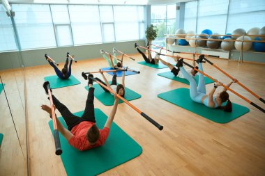 Spor yapan genç erkekler ve kadınlar spor sopasıyla jimnastik paspası tutarak spor yapıyorlar. Fitness, spor, eğitim, spor salonu ve yaşam tarzı konsepti