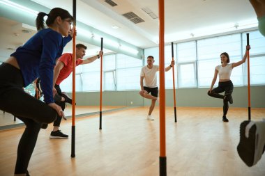 Beden eğitimi dersinde jimnastik sopaları kullanırken bacakları üzerinde dengede duran bir grup insan. Fitness, spor, eğitim, spor salonu ve yaşam tarzı konsepti