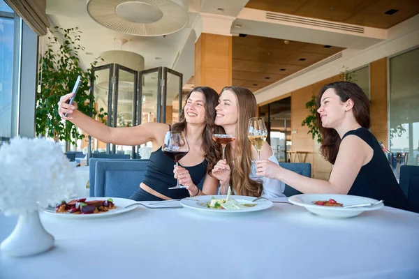 Mutlu güzel bayan, arkadaşlarıyla restoranda şampanya kadehleriyle selfie çekiyor.