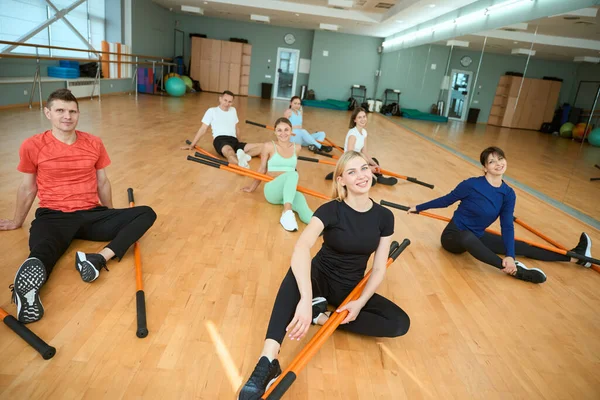 Jimnastik sopalarıyla pilates eğitimi alan insanlar spor salonunda yerde oturuyorlar. Fitness, spor, eğitim, spor salonu ve yaşam tarzı konsepti