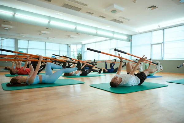Spor salonundaki spor paspasın üzerinde jimnastik sopalarıyla antrenman yapan bir grup insan. Fitness, spor, eğitim, spor salonu ve yaşam tarzı konsepti