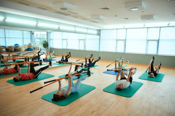 Spor salonunda jimnastik sopalarını spor minderinde uzanmış egzersiz yapan bir grup insan. Fitness, spor, eğitim, spor salonu ve yaşam tarzı konsepti