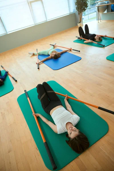 Spor minderinde uzanan jimnastik sopasıyla antrenman yapan gülümseyen genç kadınların en iyi görüntüsü. Fitness, spor, eğitim, spor salonu ve yaşam tarzı konsepti