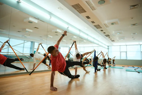 Sportif insanlar ayna duvarının arkasında eğitim ekipmanıyla egzersiz yapıyor, sıra sıra poz veriyorlar. Fitness, spor, eğitim, spor salonu ve yaşam tarzı konsepti