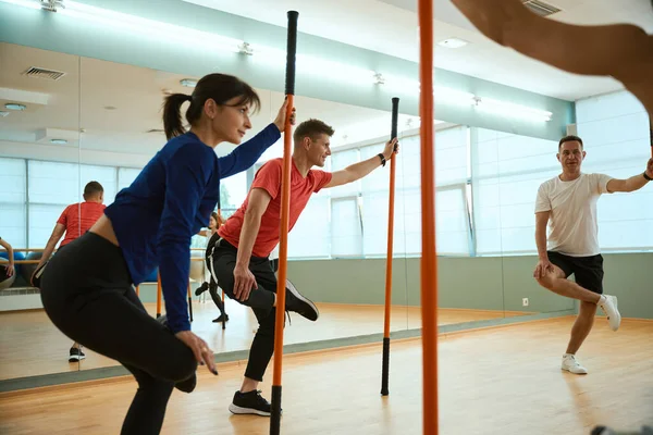 Sportif insanlar spor salonunda jimnastik sopalarını kullanırken bacakları üzerinde dengede duruyorlar. Fitness, spor, eğitim, spor salonu ve yaşam tarzı konsepti