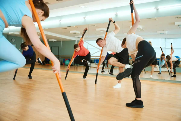 Omuzlarında jimnastik sopalarıyla dengede duran bir grup insan beden dersinde viraj yapıyor. Fitness, spor, eğitim, spor salonu ve yaşam tarzı konsepti