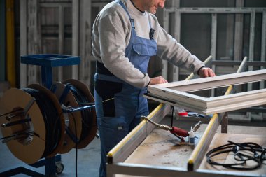 Fabrika ortamında PVC kapıları ve pencerelerin yapımında çalışan tanınmamış bir işçi.