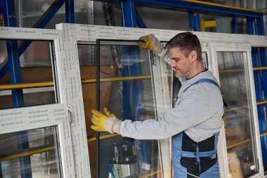 Fabrikadaki PVC kapı ve pencere montajında çalışan uzman bir erkek.