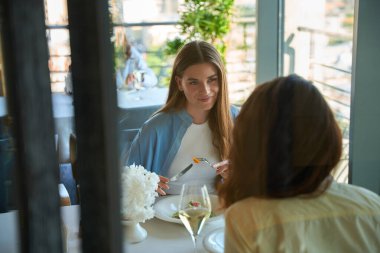 Mutlu güzel bayan, restoranda yemek yerken kız arkadaşıyla konuşuyor.