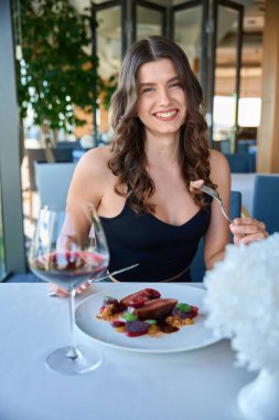 Gülümseyen genç bayan restoranda oturmuş kameraya bakarak lezzetli bifteğin tadını çıkarıyor.