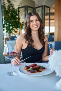 Gülümseyen güzel kadın modern restoranda biftek yerken kameraya poz veriyor.