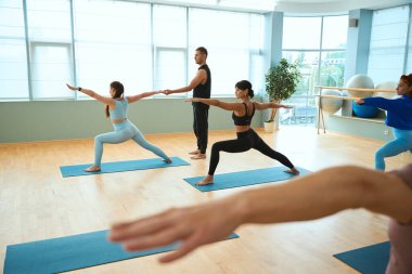 Güzel kadınlar ve erkek koç fitness stüdyosunda yoga yapıyorlar. Sağlıklı yaşam tarzı, spor, jimnastik, yoga stüdyosu