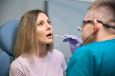 KBB doktoru klinikte genç bir kadının boğazını muayene ediyor. Ağzını gırtlağına kadar açıyor. Otolaryngology konsepti