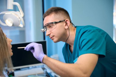 Erkek otolarolog klinikte genç bir kadının boğazını incelemek için spatula kullanıyor. Otolaryngology konsepti