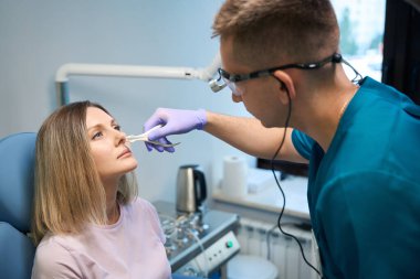 Erkek otorhinolaringolog, tıp merkezindeki kadın hastasının otoskopuyla burnunu kontrol ediyor. Otolaryngology konsepti