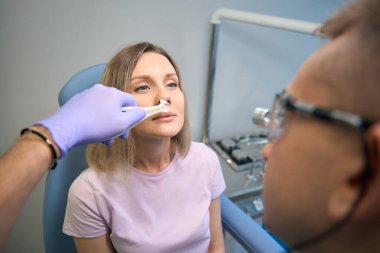 Erkek laringolog, tıp merkezindeki genç bayan hastanın otoskobuyla burnunu kontrol ediyor. Otolaryngology konsepti