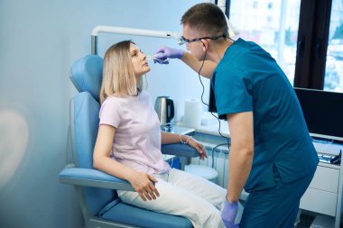 Erkek doktor ent, tıp merkezindeki genç bayanın burun muayenesi yapıyor. Otolaryngology konsepti