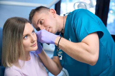 Erkek otolargolog, tıp merkezinde otoskop kullanarak genç bir kadının kulağını kontrol ediyor. Otolaryngology konsepti