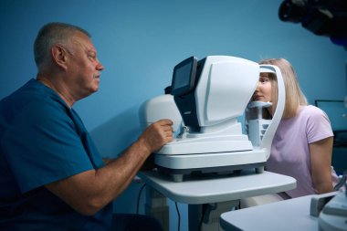 Göz hekimliği kliniğinde yaşlı bir doktor gözlerini muayene ettiriyor. Optometri kavramı