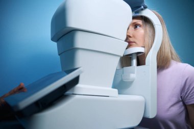 Göz doktoru kliniğindeki göz testi makinesine bakan bir kadın hasta. Tıp, sağlık hizmeti kavramı