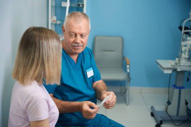 Yetişkin erkek göz doktoru göz hekimliği kliniğinde kadın hastayla konuşuyor.