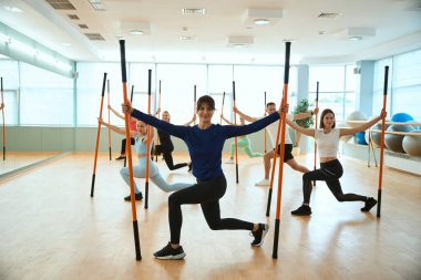 Spor salonundaki erkekler ve kadınlar jimnastik çubukları kullanarak denge egzersizleri yapıyorlar. Fitness, spor, eğitim, spor salonu ve yaşam tarzı konsepti